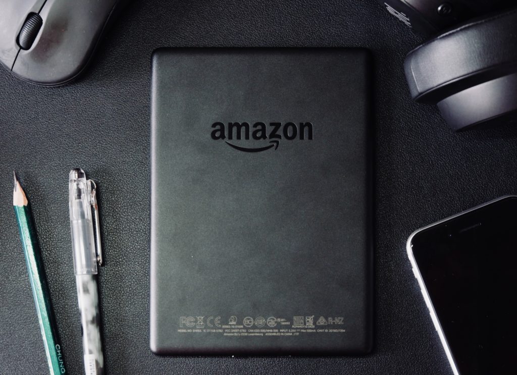 tablet preto com logotipo da amazon com caneta, lapis e telemovel ao lado